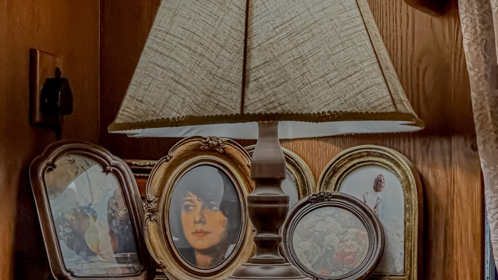 A quiet domestic interior — lamp, books, the small artifacts of a settled household. The substrate of formation.